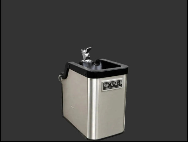 A stainless steel outdoor water fountain with a black top rim, a metal spout, and a visible BACKYARD brand badge on the front, shown against a dark gray background.
